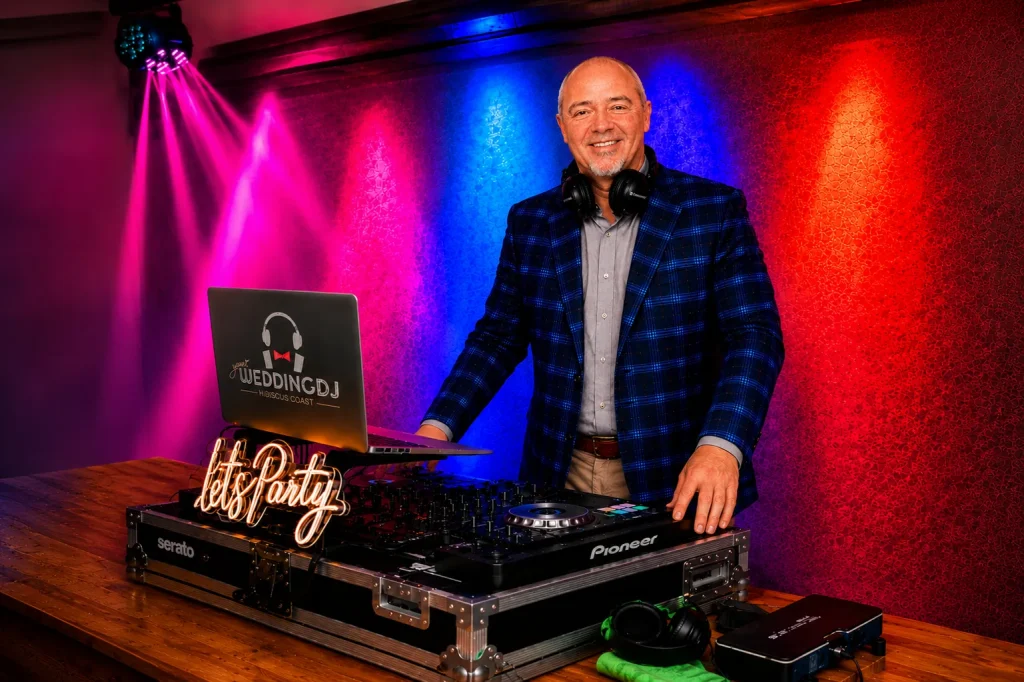 Meet DJ Timo portrait at a luxury wedding reception, standing behind professional DJ equipment in a blue check blazer